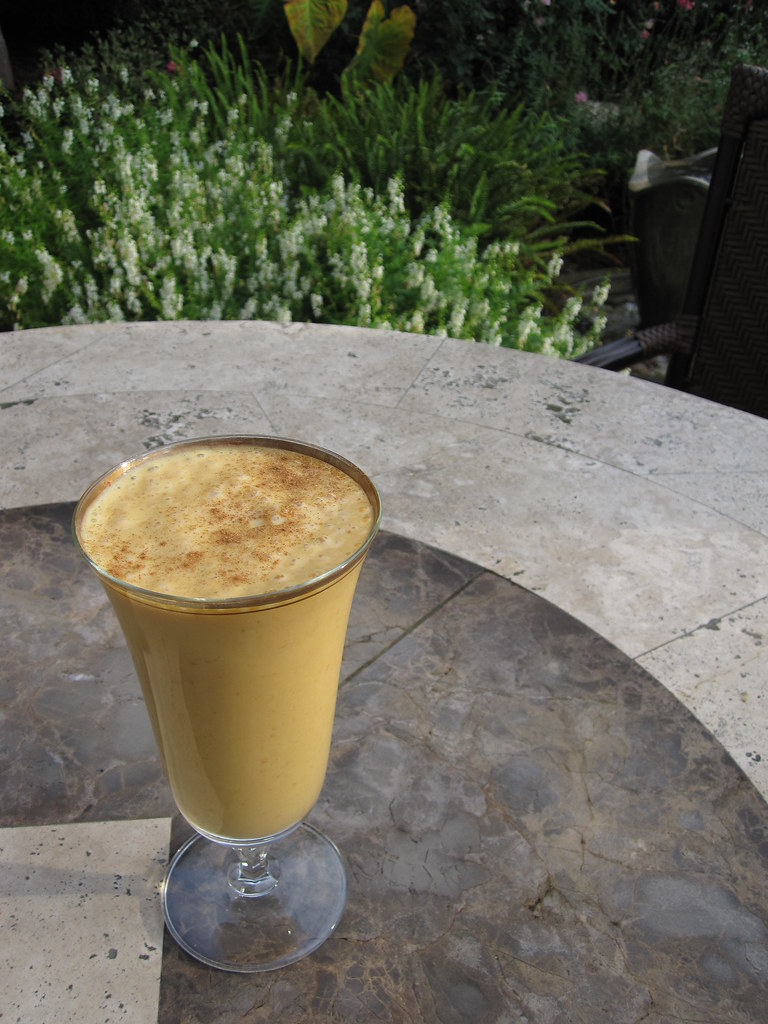 A tall glass of pumpkin smoothie on an outdoor table.