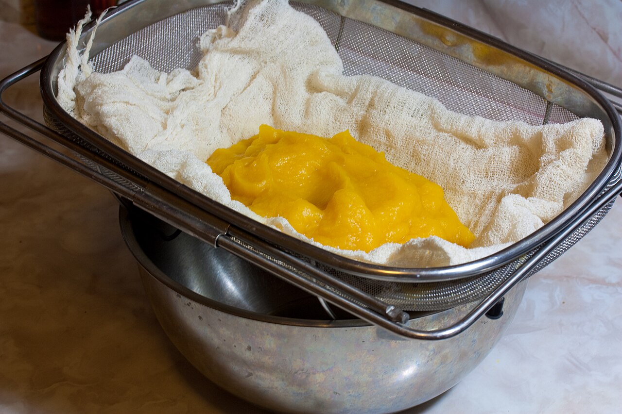 Bright pumpkin puree draining in cheesecloth set over a bowl.