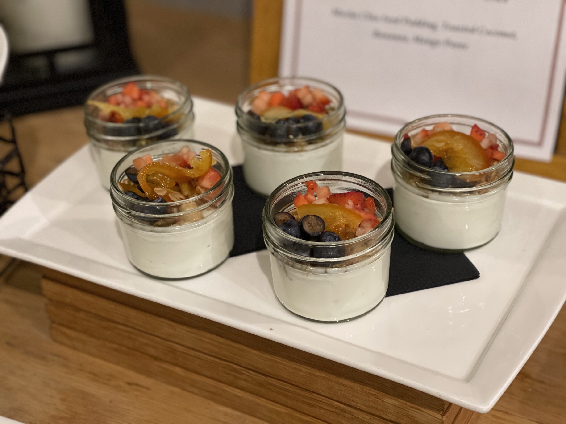 Several small yogurt parfait jars topped with berries and citrus on a serving tray.