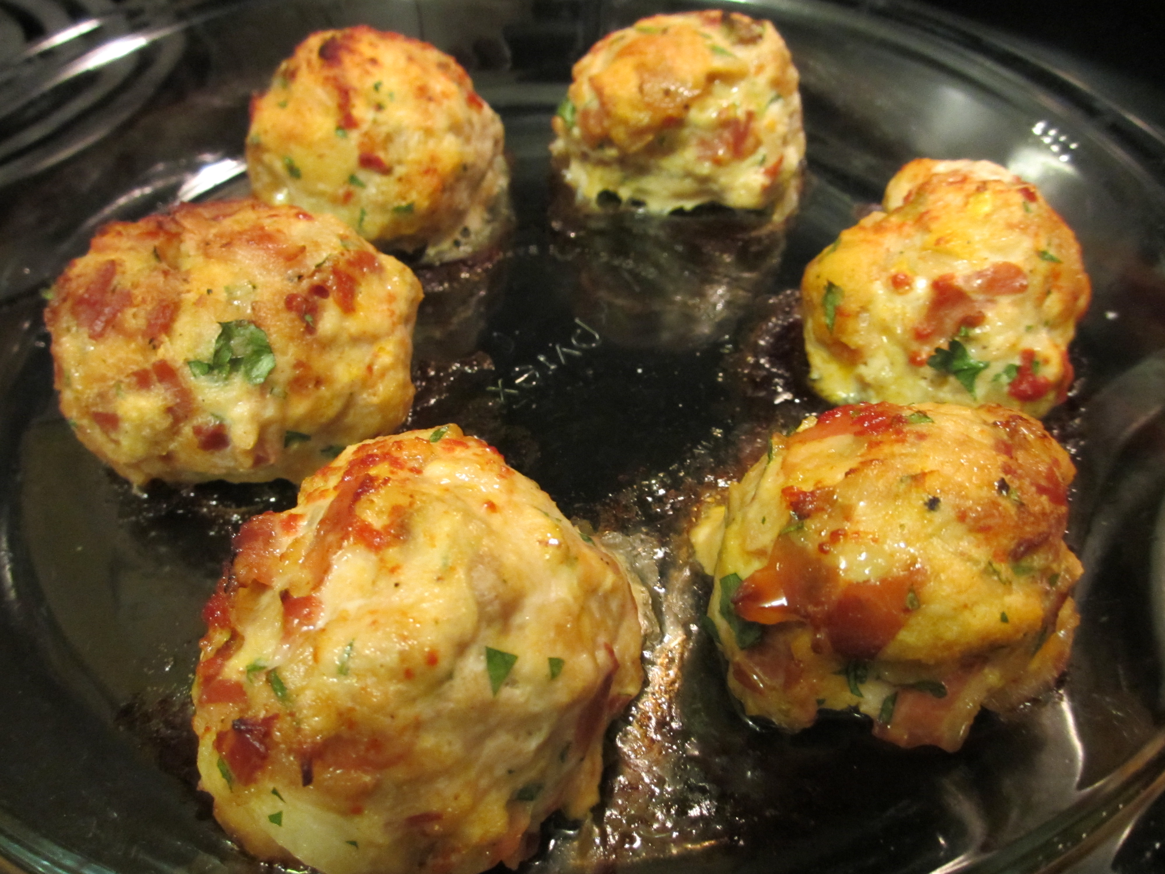 Golden baked chicken meatballs in a skillet, flecked with herbs and tomato.