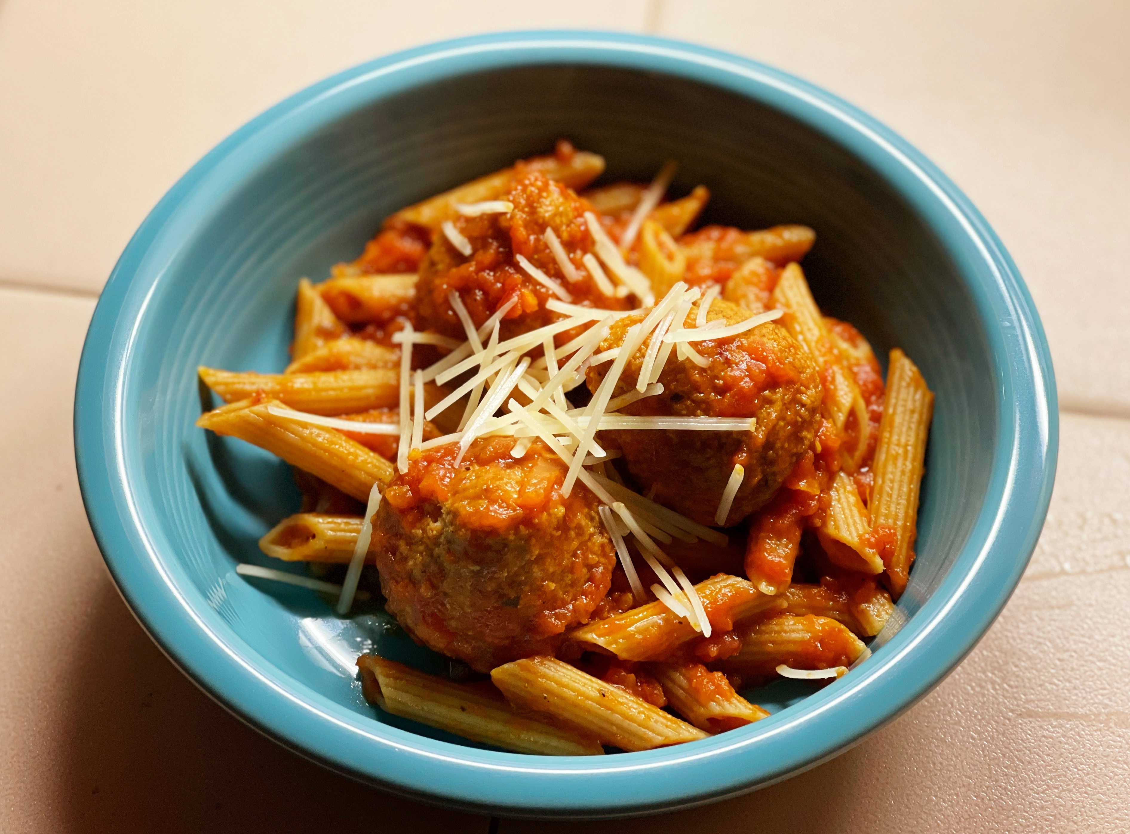 Penne pasta with turkey meatballs, tomato sauce, and shredded cheese in a blue bowl.
