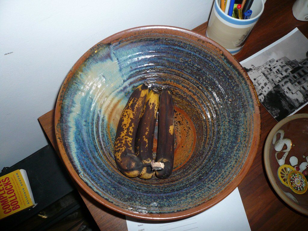 Very ripe bananas with dark peels resting in a large ceramic bowl.