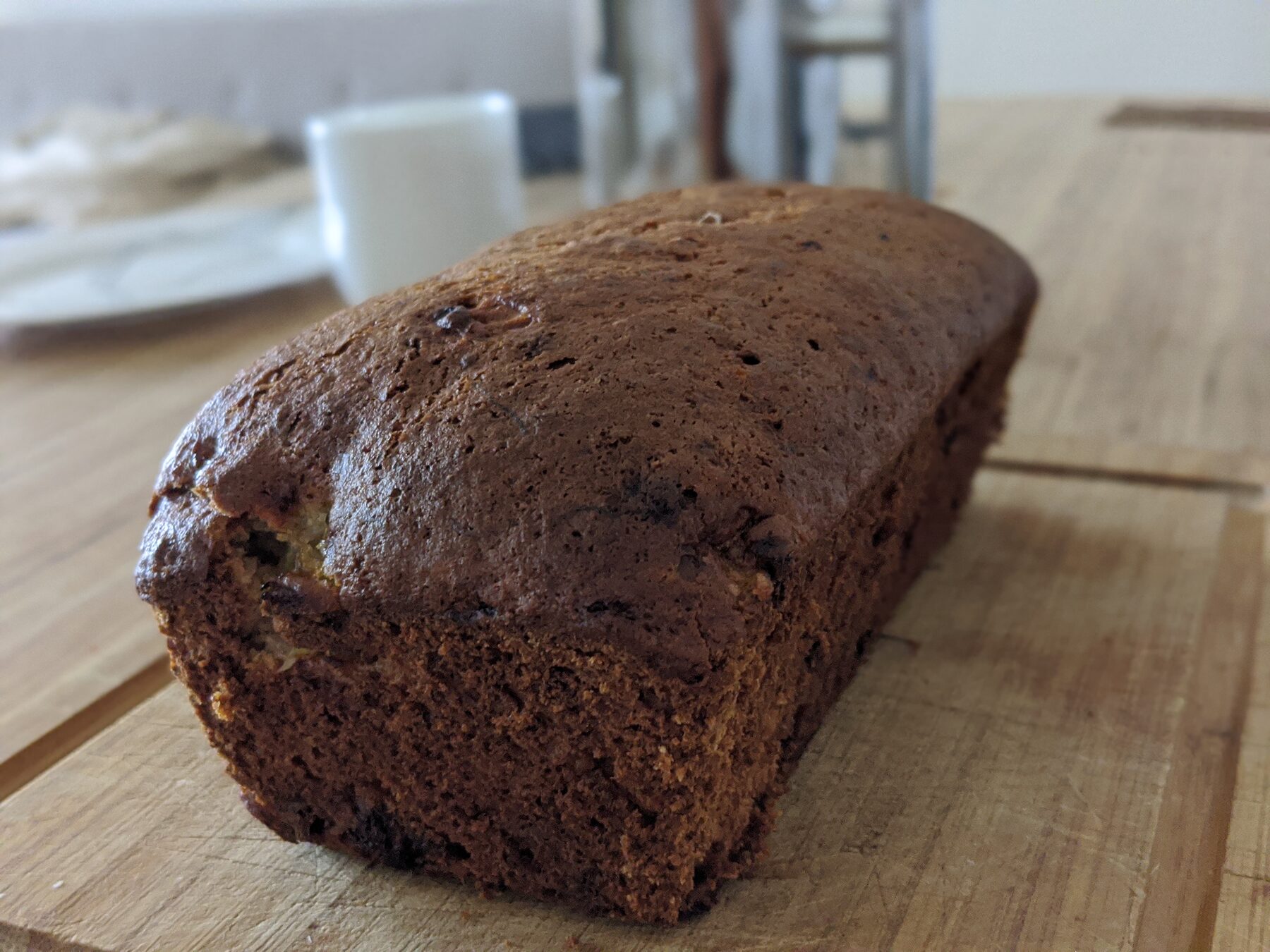 An unsliced loaf of banana bread cooling on a wooden cutting board.