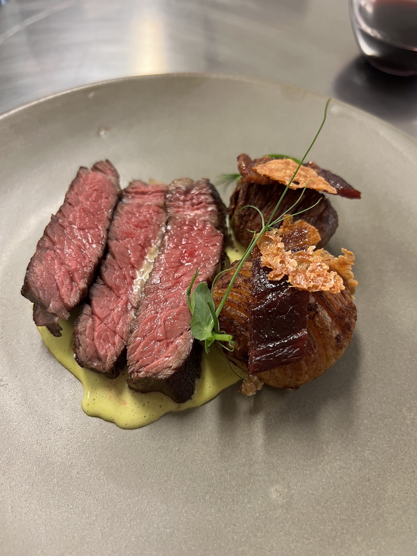 A plated meal with garlic Hasselback potatoes beside steak and sauce.