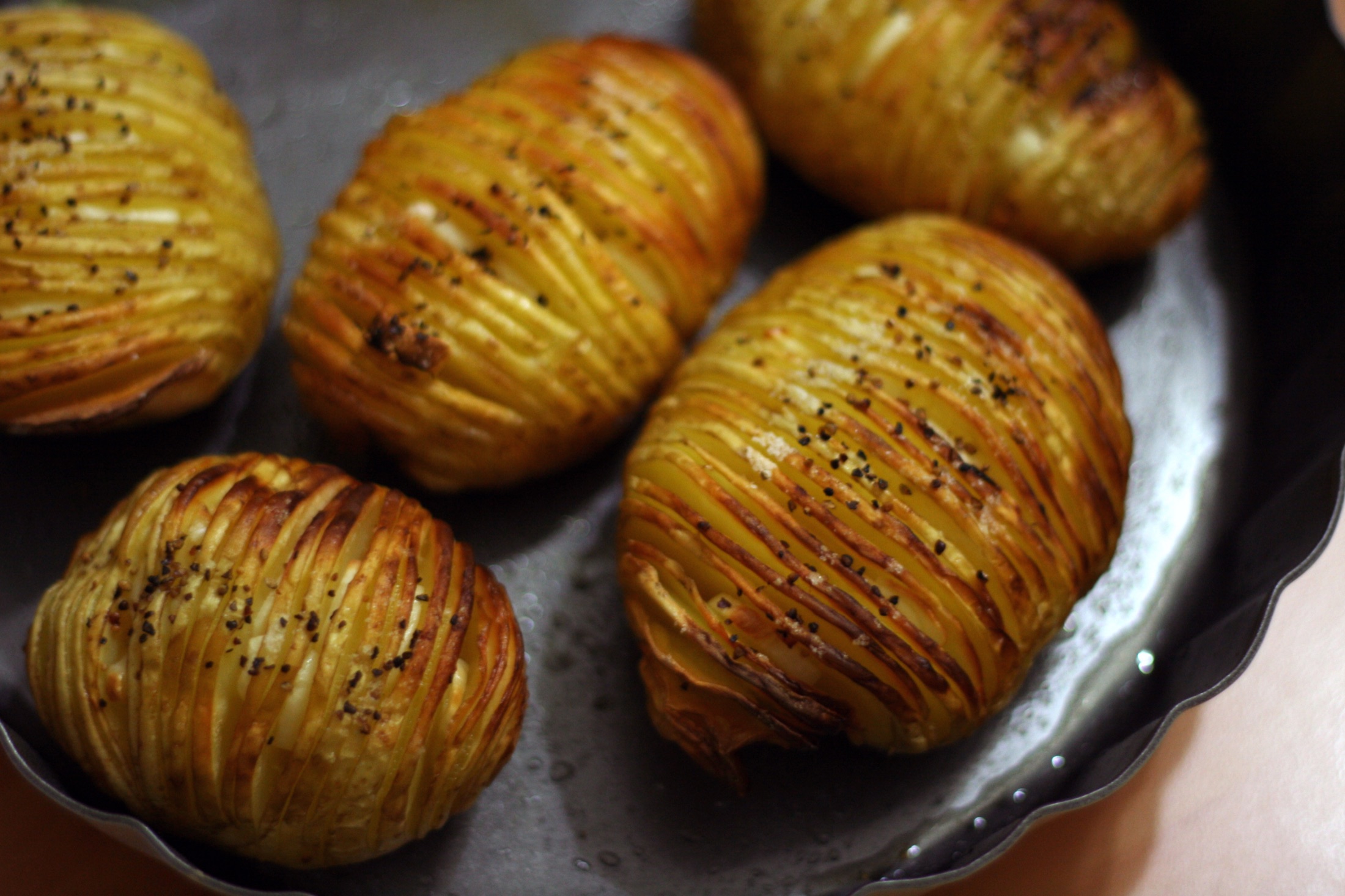 Golden Hasselback potatoes baked in a dark tray with their sliced tops fanned open.