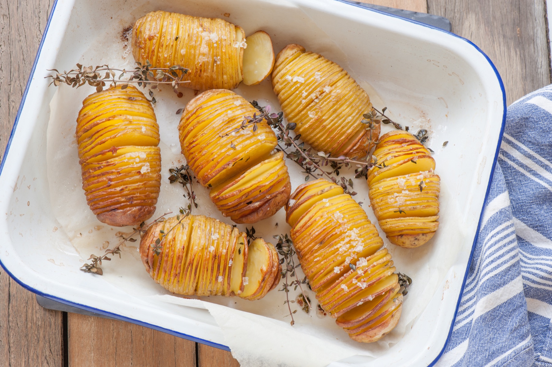 A small roasting dish with three deeply browned Hasselback potatoes.