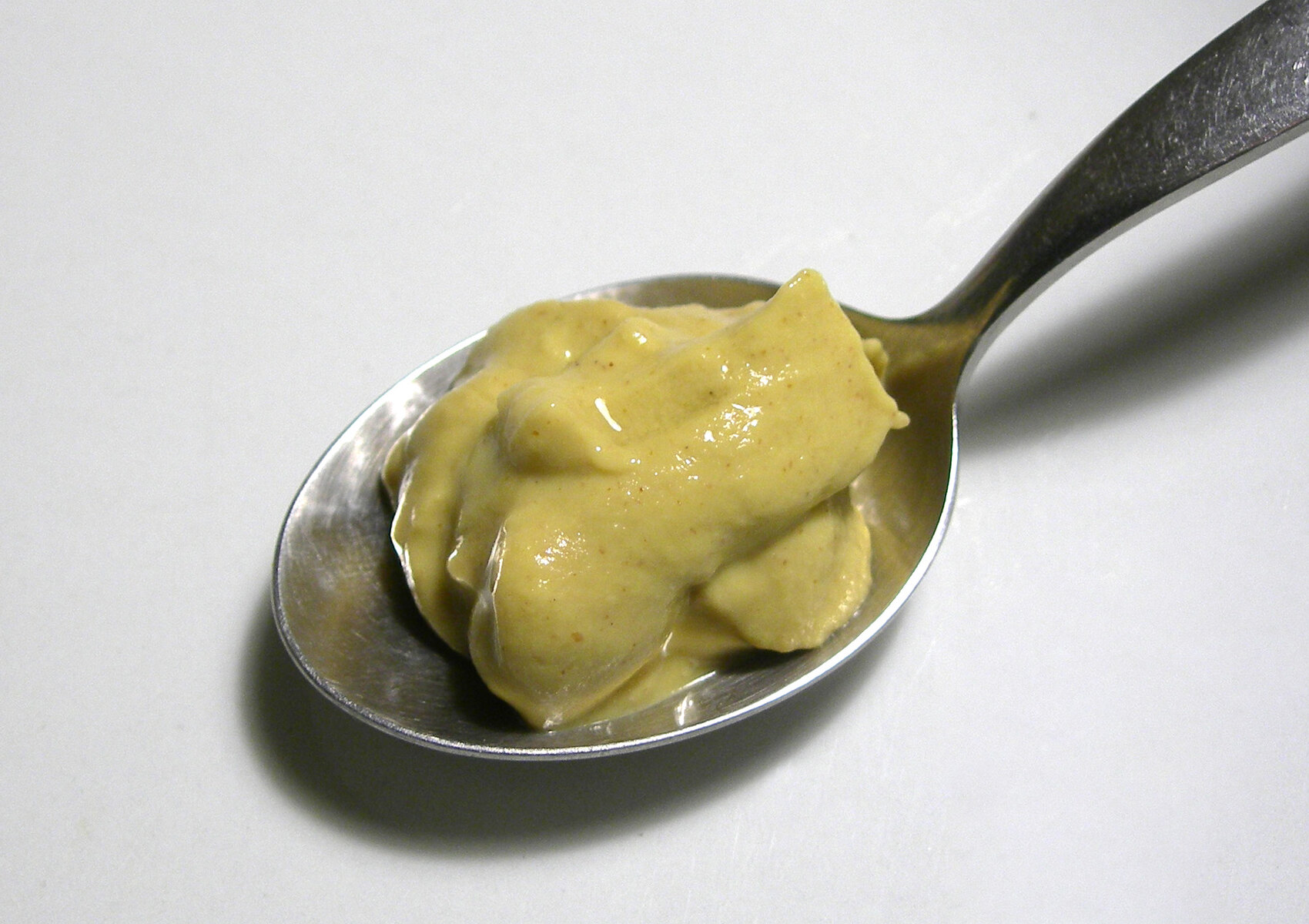Dijon mustard mounded on a spoon against a pale background.