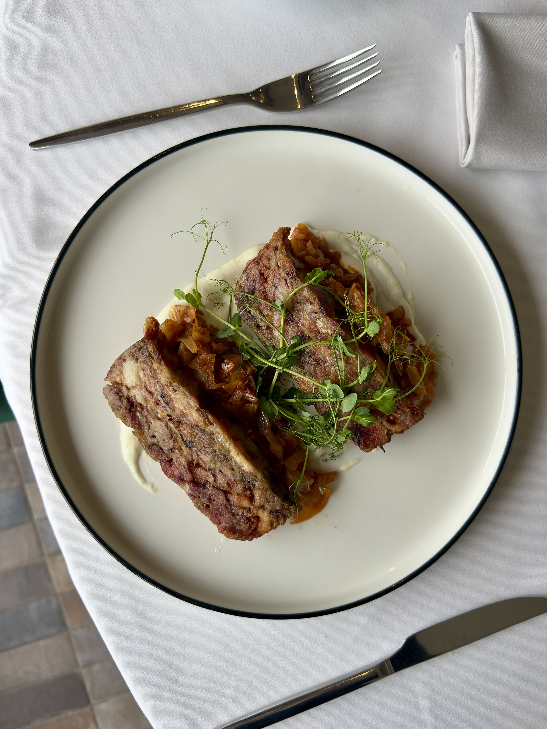 A restaurant-style plate of sliced meatloaf with sauce, herbs, linen, and polished silverware.