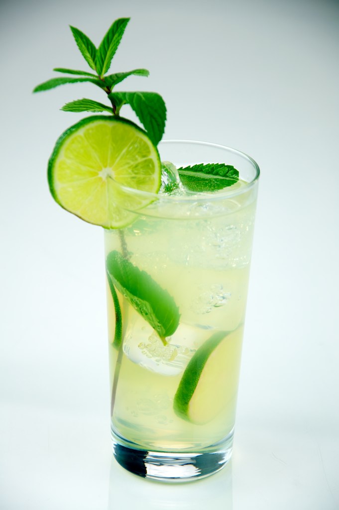 A tall mixed drink with lime, mint, ice, and club soda bubbles.